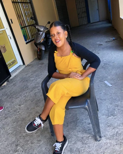 A smiling girl in a yellow outfit sitting outdoors